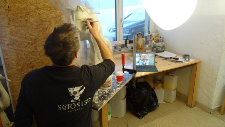 Handwerker modelliert 3D Tierziel im Atelier mit Laptop und Werkzeugen
